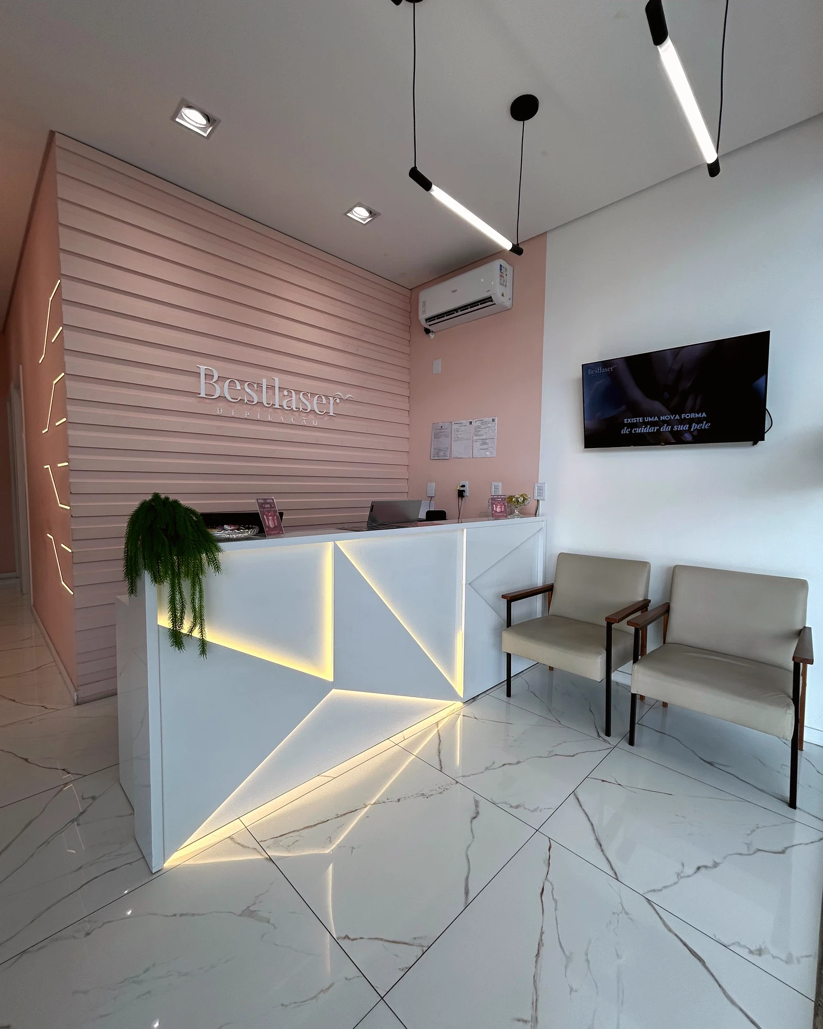Recepção real da Bestlaser com balcão iluminado, parede rosa e poltronas.